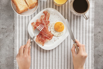 Young woman eating fried egg and bacon at table