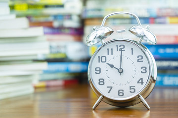Alarm clock on wooden table with blurred pile of book as background