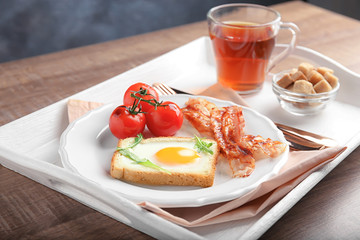 Plate with fried egg, bacon and tomatoes on tray