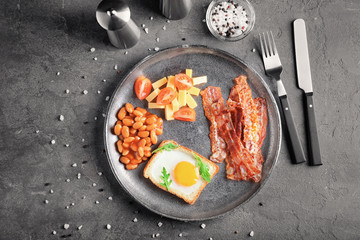 Plate with fried egg, bacon and beans on table