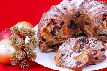 isolated traditional christmas stollen cake, sweet german bread, with dried fruits on white plate and red background with christmas decoration
