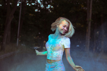 Joyful young woman in white t shirt with fluttering hair posing with Holi powder