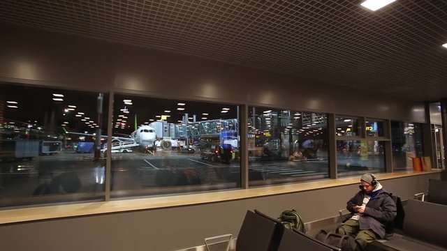 Man is sitting in departure lounge waiting for flights and plane in the window