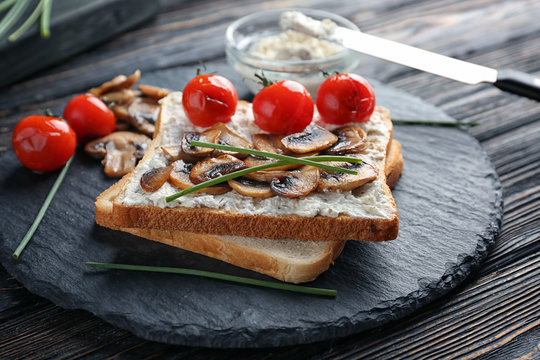 Slate plate with tasty toasts, cheese and vegetables on table