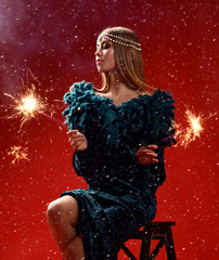 Beautiful fashion woman holding two sparklers in dark green dress on red christmas 