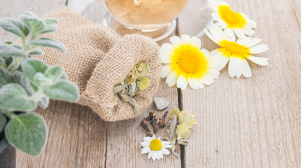 Cup of chamomile tea with chamomile and pouch with herbs on rustic wooden background. Herbal tea flowers and dittany.