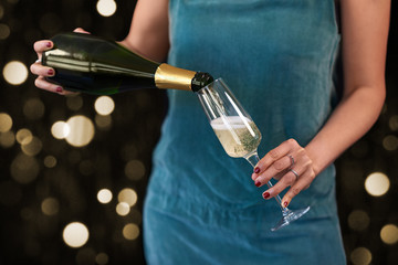 Anonymous woman hands pouring champagne in to glass with bubbles