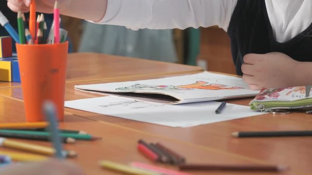 Close-up of unknown little girl draws the pictures using color pencils in the album in the kindergarten