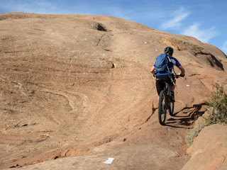 Obraz premium Mountain biker climbing a sandstone hill at Slickrock mountain biking trail in Moab, Utah