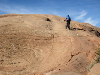 Obraz premium Mountain biker climbing a sandstone hill at Slickrock mountain biking trail in Moab, Utah