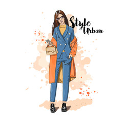 Urban style. Hand drawn sketch. Young stylish woman in a pantsuit and coat. In the hand of a woman holding a gadget and bag. Vector illustration.