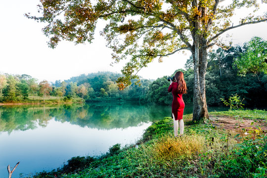 The girl wearing a red dress photographed the maple leaf in autumn