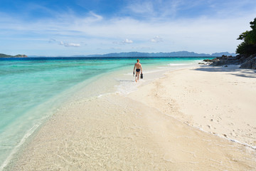 Man with snorkeling mask and flippers walking on the beautiful beach.