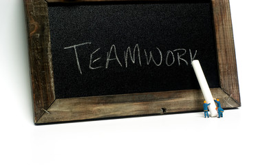 Teamwork - Miniature construction worker figurines posed as if writing "Teamwork" on a chalkboard.