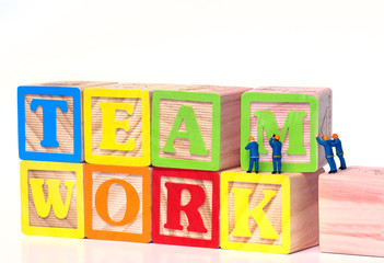 Teamwork - Miniature construction worker figurines posed as if building the word Teamwork with toy blocks.