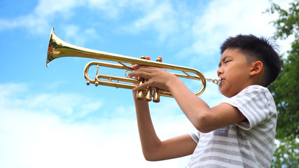 Asian boy playing trumpet with blue sky background.