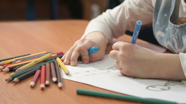 Close-up of unknown little girl draws the pictures using color pencils in the album in the kindergarten