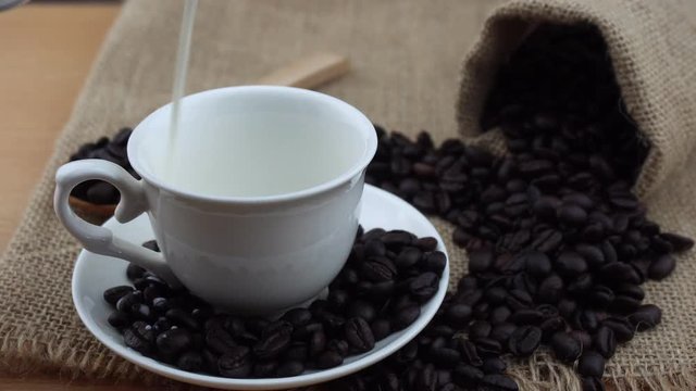 Pouring milk into a coffee cup with coffee beans on sack bag