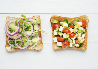 Two avocado toasts on white wooden background