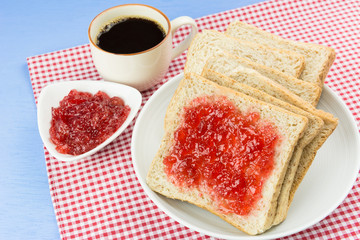 whole wheat bread with strawberry jam and cup of coffee on cotton fabric.