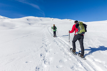 Fototapeta na wymiar Senior couple is snowshoe hiking in alpine winter mountains. Bavaria, Germany.