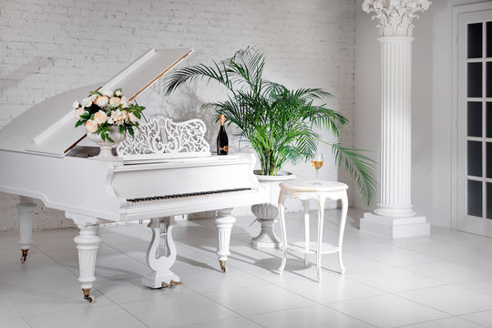 Grand piano in a luxury white classic interior with wine, palms and flowers.