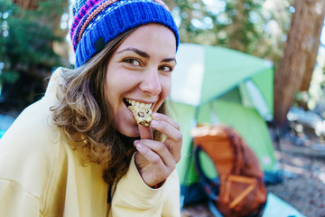 Smiling woman tourist eating snack and camping in the wild