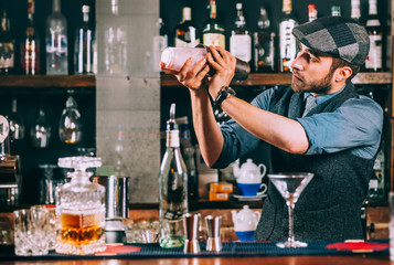 Portrait of barman preparing cocktails, using shaker and pouring beverages