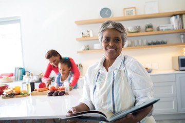 Portrait of smiling senior woman holding recipe book in kitchen