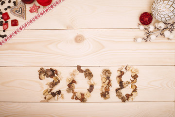 2018 inscription of dried flowers with traditional Christmas ornaments in white and red colors. a light wooden background. Top view. Copyspace.