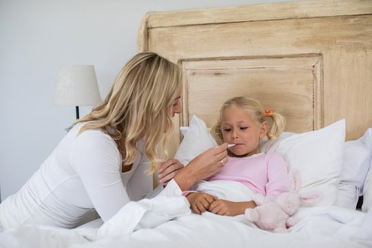 Mother checking sick daughter temperature with digital