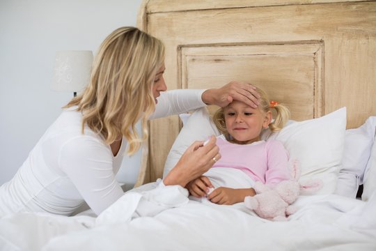 Mother checking sick daughter temperature with digital - Powered by Adobe