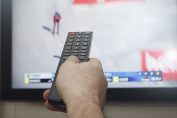 мужская рука с пультом управления на фоне  телевизора со спортивной передачей