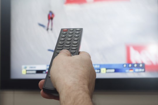 мужская рука с пультом управления на фоне  телевизора со спортивной передачей