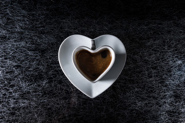 A heart shaped coffe cup with black coffee on a black and silver kitchen table top in hard, low key light - 183452326
