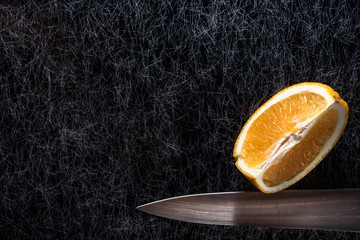 An orange fruit with a carving knife silver blade on a black and silver kitchen table top in hard, low key light - 183452527
