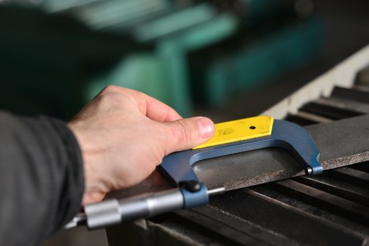 Elderly worker looks in the drawing to see detail sizes. The man turner measures the dimensions of the part on a micrometer, and also uses a sliding caliper.