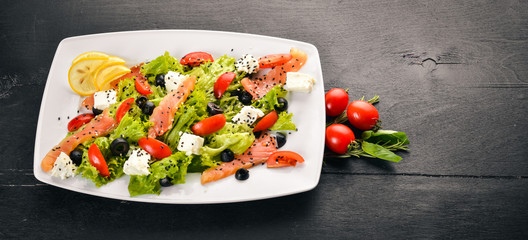 Salmon salad, feta cheese, salad leaves and fresh vegetables on the plate. On a wooden background. Top view. Free space for text.