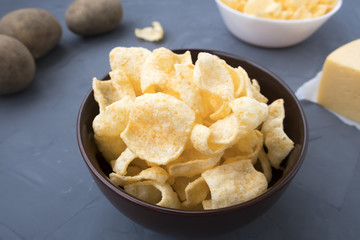 Potato chips with cheese in a plate that is located on a gray background.