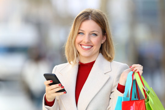 Shopper holding shopping bags and phone looking at camera