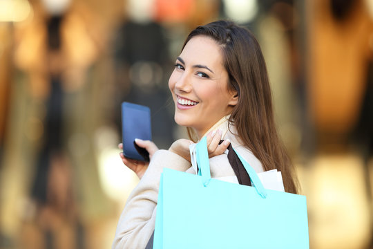 Shopper holding phone and shopping bags looking at you