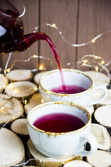 Red tea karkade with berries in a transparent teapot pours into the cup on a wooden table. Rustic style