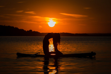 Silhouette of beautiful young girl exercising yoga on SUP in the scenic yellow sunset on lake Velke Darko, Zdar nad Sazovou, Czech republic