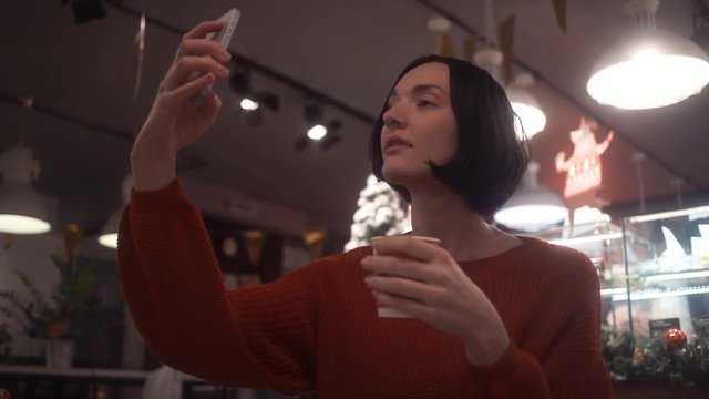Attractive woman wearing jumper sitting in cafe using smartphone taking selfie