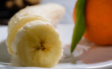 Sliced banana on a white plate with mandarin orange in the background