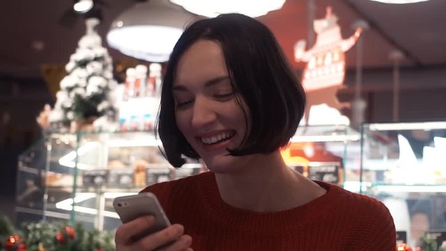 Happy young woman smiling texting message using smartphone sitting in cafe.