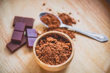 Dark chocolate with cocoa powder on wooden table