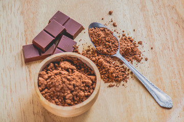 Dark chocolate with cocoa powder on wooden table