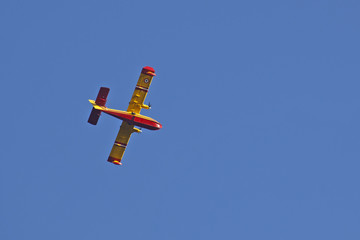 Avion Canadair rouge et jaune de lutte contre les incendies vu du dessous sur fond de ciel bleu.