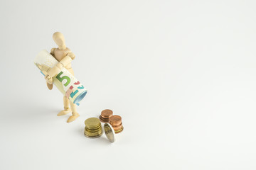 Holzfigur mit einem B&uuml;ndel Geldscheine unter dem Arm, M&uuml;nzgeld daneben, freigestellt und Textfreiraum